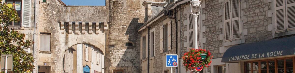 Eine Kopfsteinpflasterstraße mit historischen Steinbauten, einem Schild für 'L'Auberge de la Roche' und einer Fußgängerüberweg.
