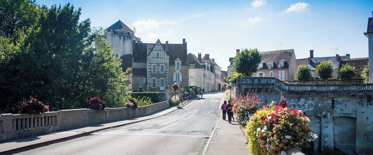 A historic town with cobblestone streets, traditional buildings, and a bridge with flower baskets.