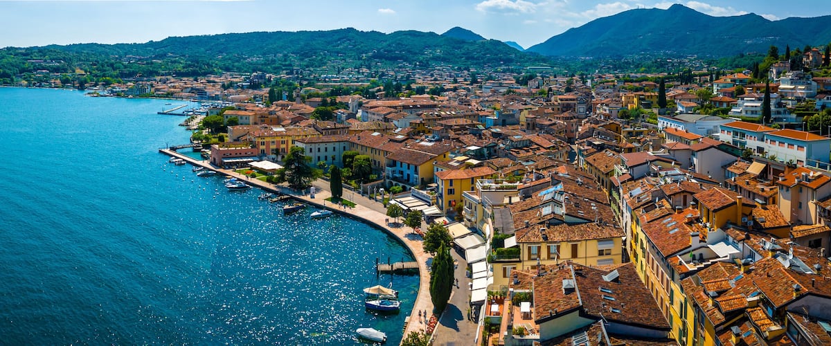 A coastal town with a marina, terracotta-roofed buildings, and mountains in the background.