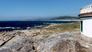 A coastal landscape with rocky terrain, a white building with a green door, and the ocean in the background.