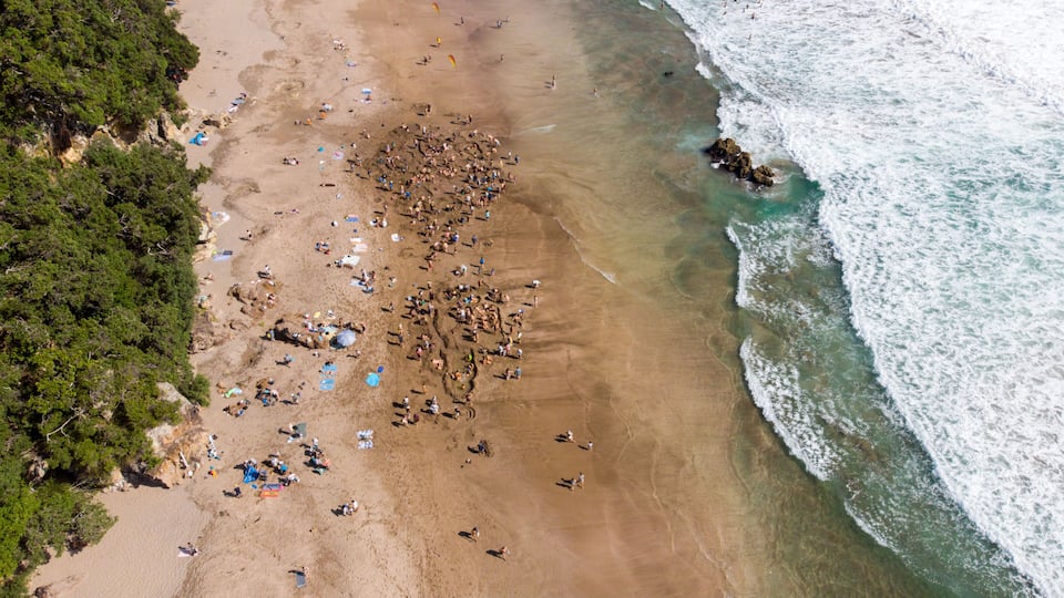 An aerial view of a beach with people, tents, and a rocky outcrop near the water.