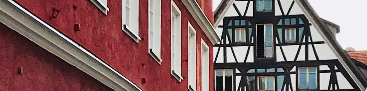 Un bâtiment rouge aux encadrements de fenêtres blancs, avec, en arrière-plan, un bâtiment à colombages noir et blanc.
