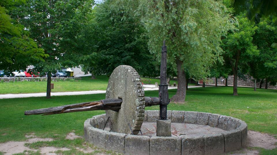 A historical water pump in a park surrounded by trees and grass.