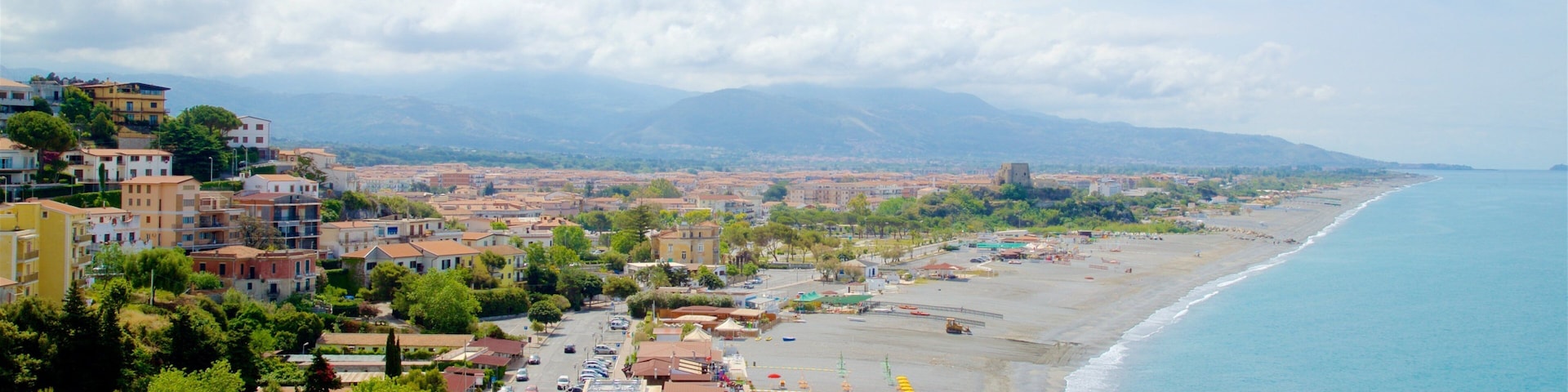 A coastal town with a beach, buildings, and mountains in the background.