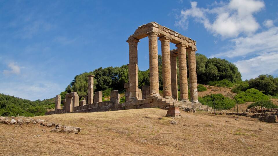 Ancient stone columns on a hillside with a clear blue sky.