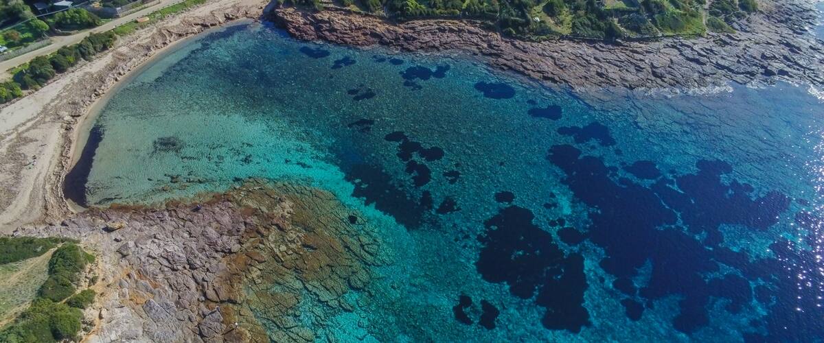 An aerial view of a coastal area with clear turquoise waters, rocky shorelines, and scattered buildings.