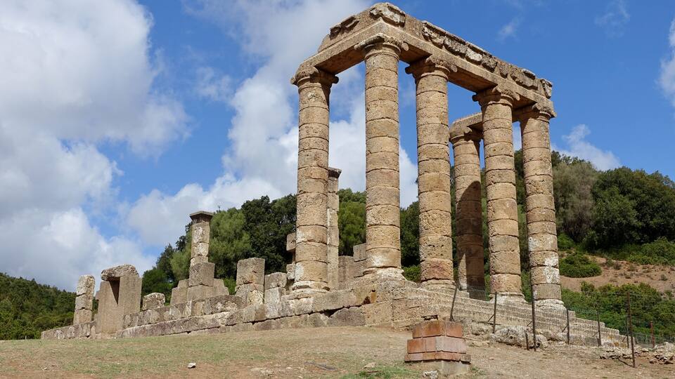 Ancient stone columns and ruins on a hillside with a clear sky.