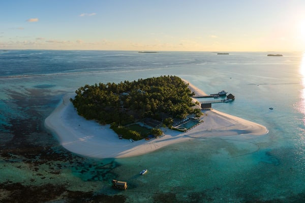 Eine Luftaufnahme einer tropischen Insel mit klarem türkisblauem Wasser, einem Sandstrand und einem kleinen Steg.