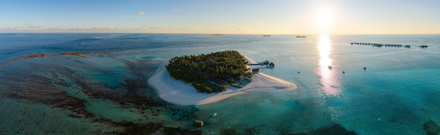 Vista aérea de una isla tropical con aguas turquesas cristalinas, una playa de arena y un pequeño muelle.