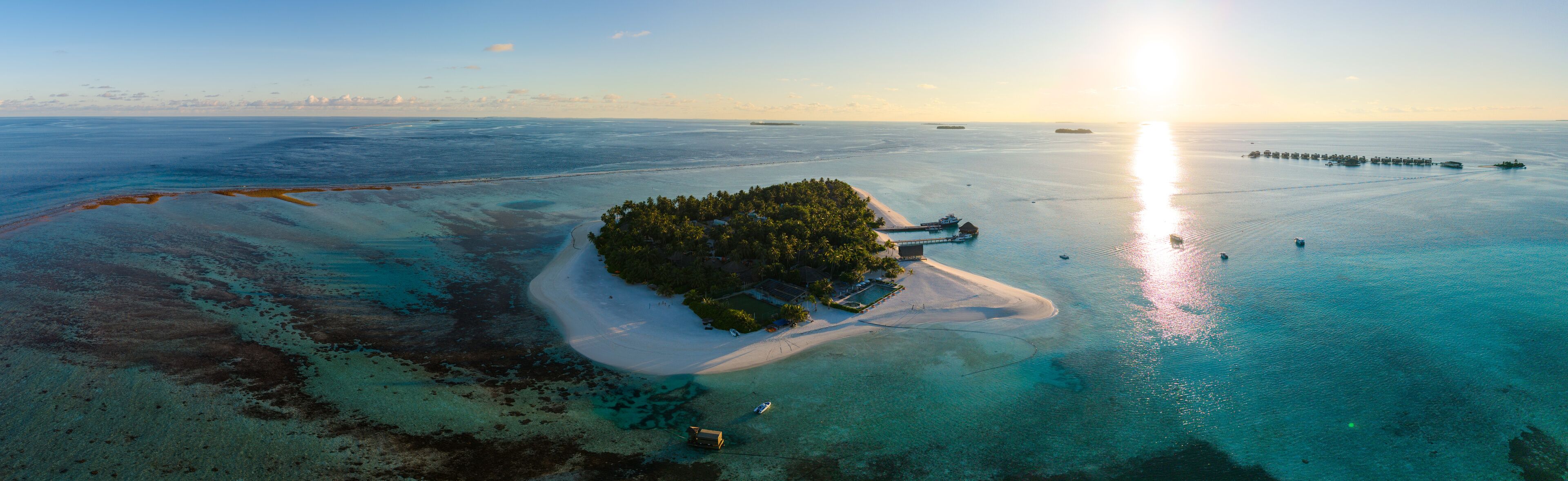 An aerial view of a tropical island with clear turquoise waters, a sandy beach, and a small dock.