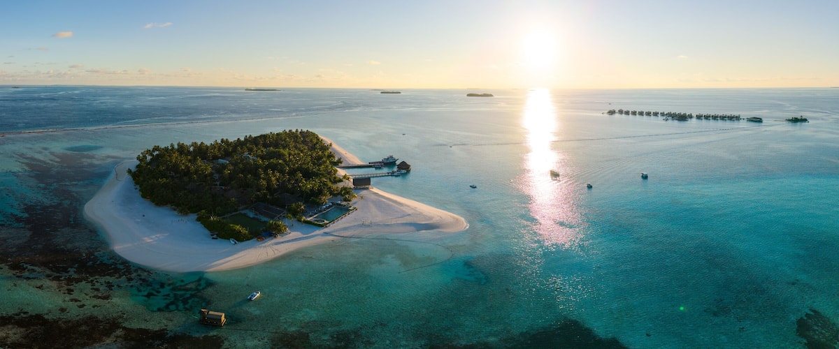 An aerial view of a tropical island with clear turquoise waters, a sandy beach, and a small dock.