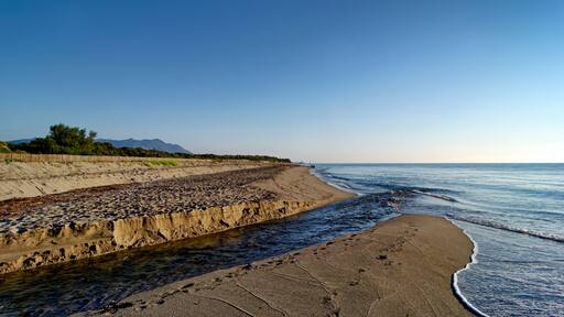 Eine Küstenlandschaft mit Sandstrand, felsiger Küste und blauem Himmel.