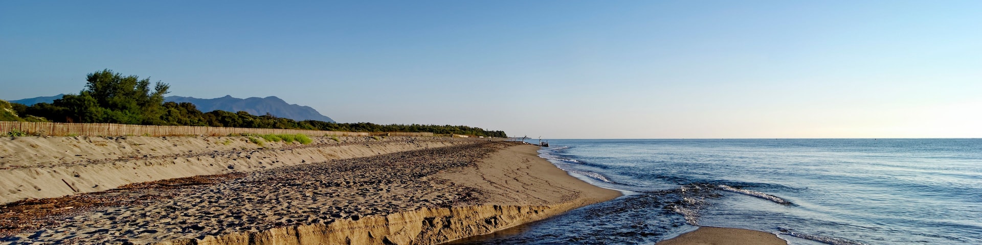 Un paisaje costero con una playa arenosa, un litoral rocoso y un cielo azul despejado.