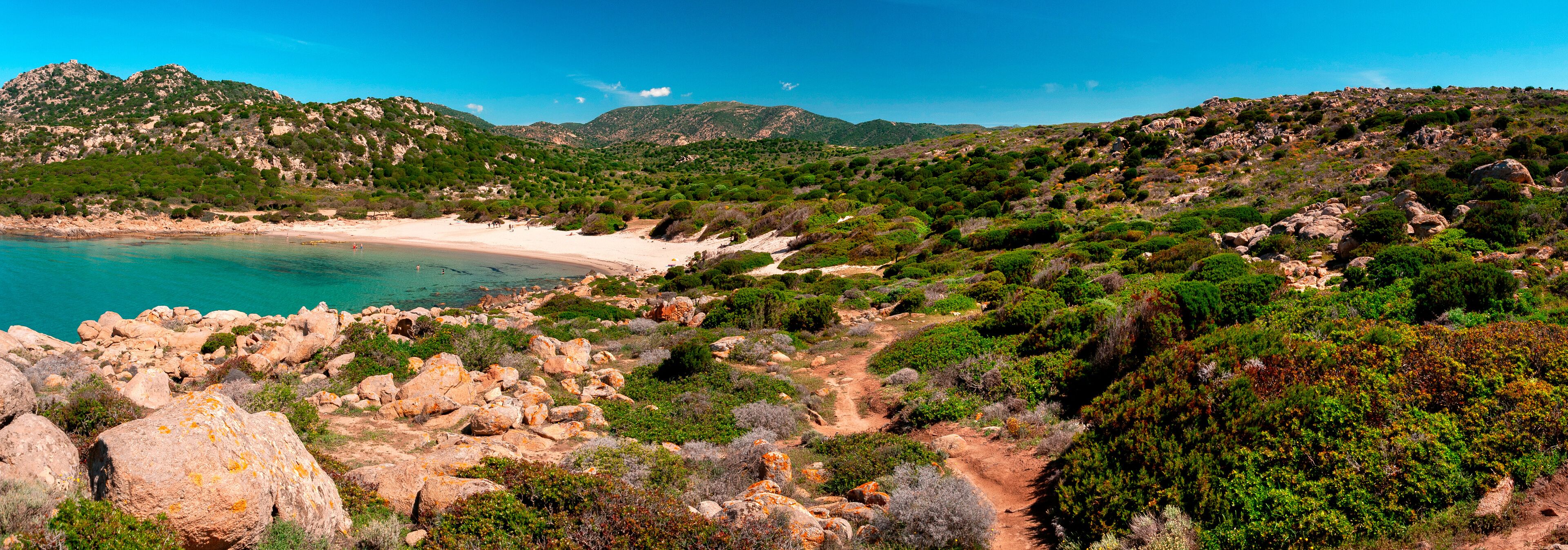 A coastal landscape with a sandy beach, rocky terrain, and dense greenery.