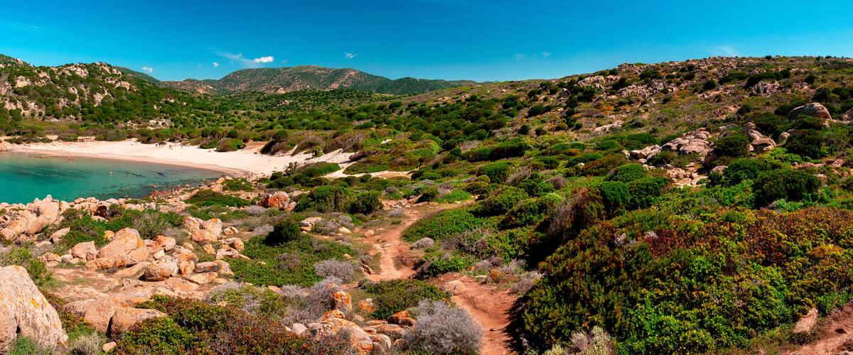 A coastal landscape with a sandy beach, rocky terrain, and dense greenery.