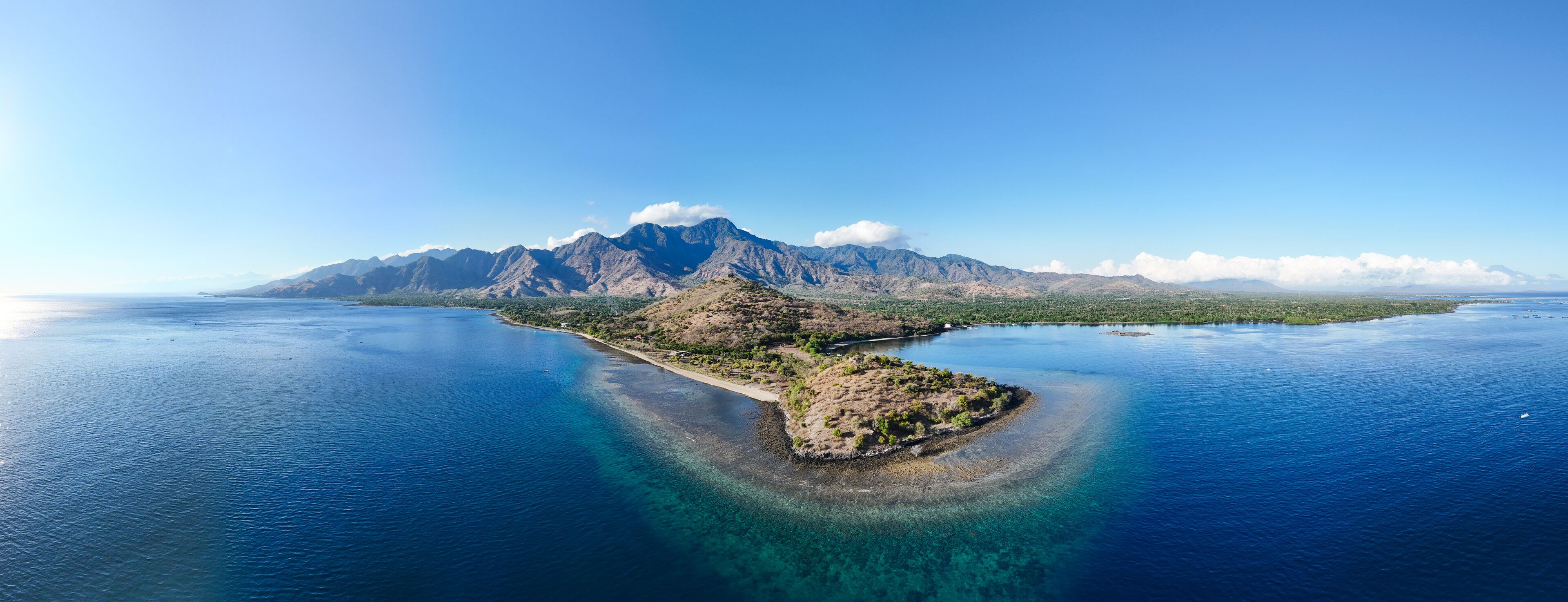 Aerial view of dramatic mountains meeting the serene ocean, with a sunlit peninsula, Pemuteran, Bali, Indonesia.