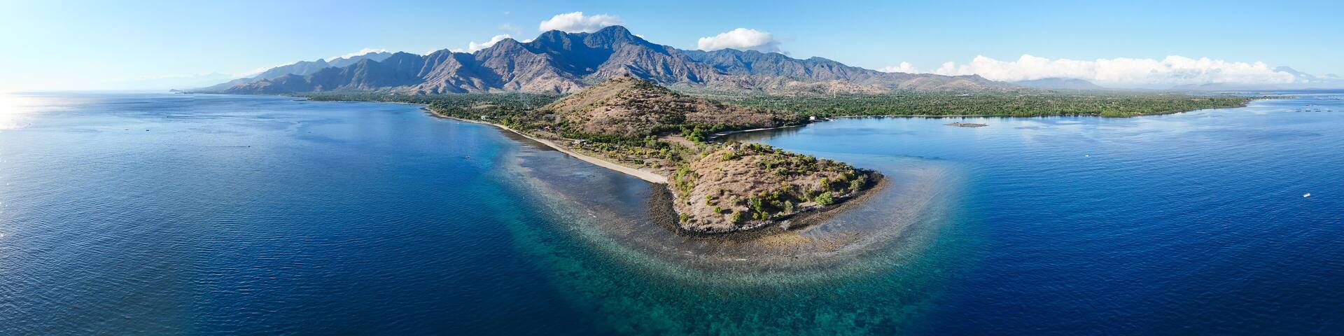 A coastal landscape with a prominent mountain range and a small island with clear blue waters.