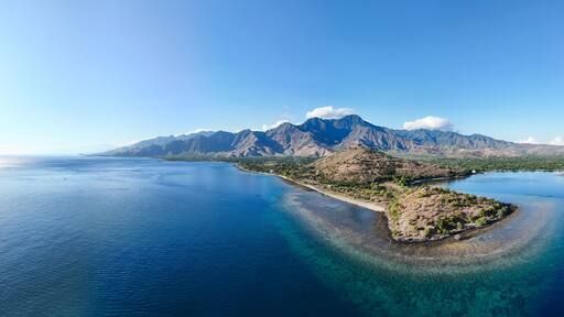Aerial view of dramatic mountains meeting the serene ocean, with a sunlit peninsula, Pemuteran, Bali, Indonesia.