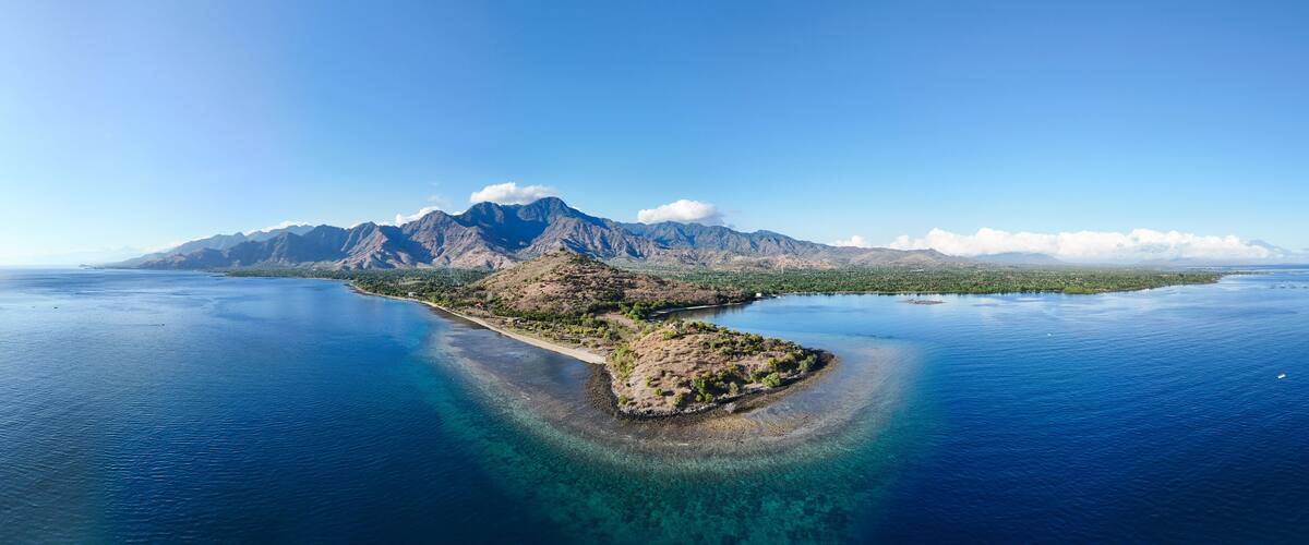 A coastal landscape with a prominent mountain range and a small island with clear blue waters.