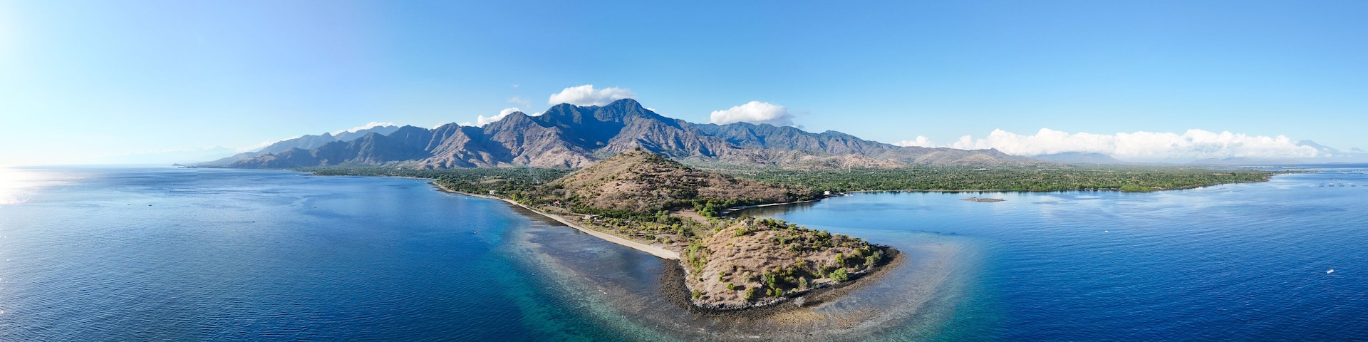 A coastal landscape with a prominent mountain range and a small island with clear blue waters.