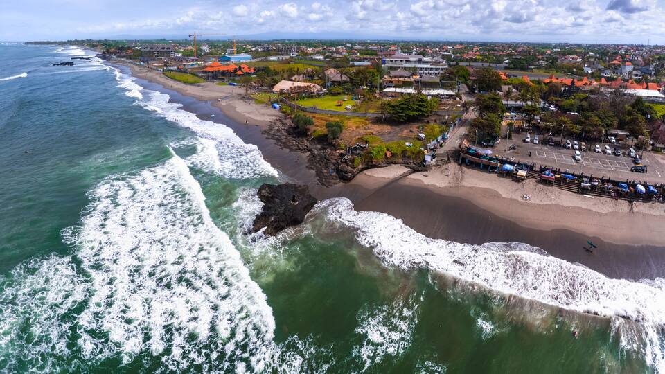 A coastal town with a beach, ocean waves, and a mix of residential and commercial buildings.