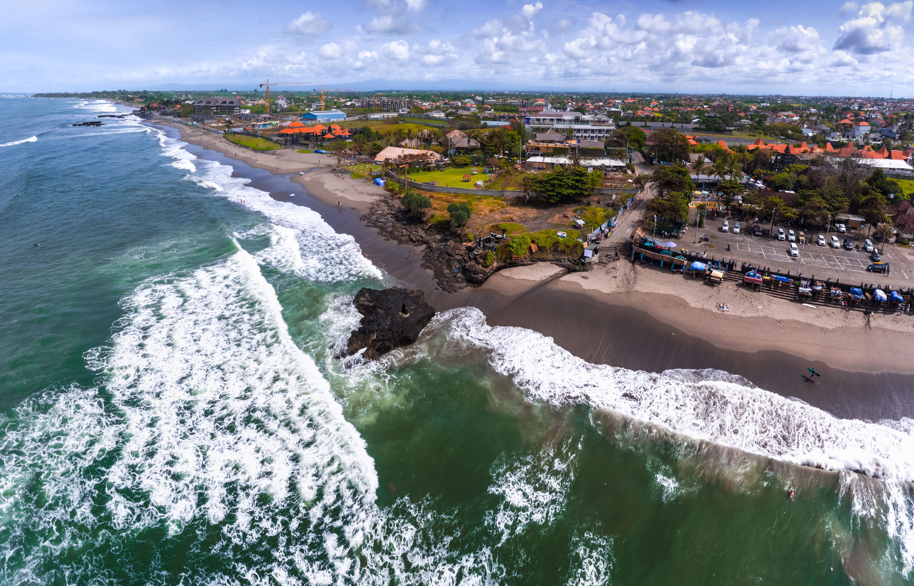 A coastal town with a beach, ocean waves, and a mix of residential and commercial buildings.