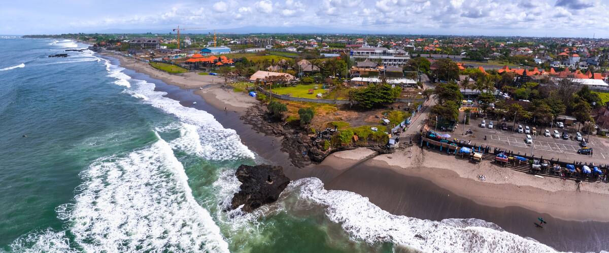 A coastal town with a beach, ocean waves, and a mix of residential and commercial buildings.