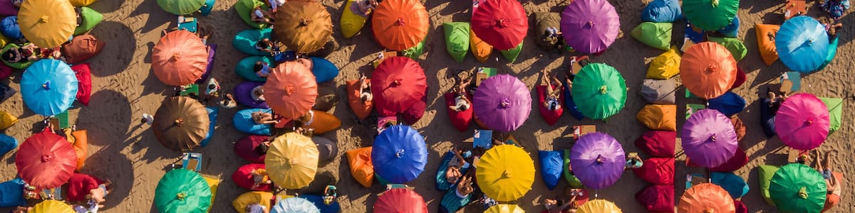 A beach with numerous colorful umbrellas and people relaxing.
