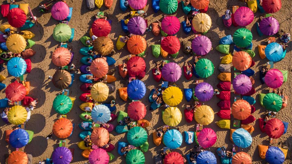 A beach with numerous colorful umbrellas and people relaxing.