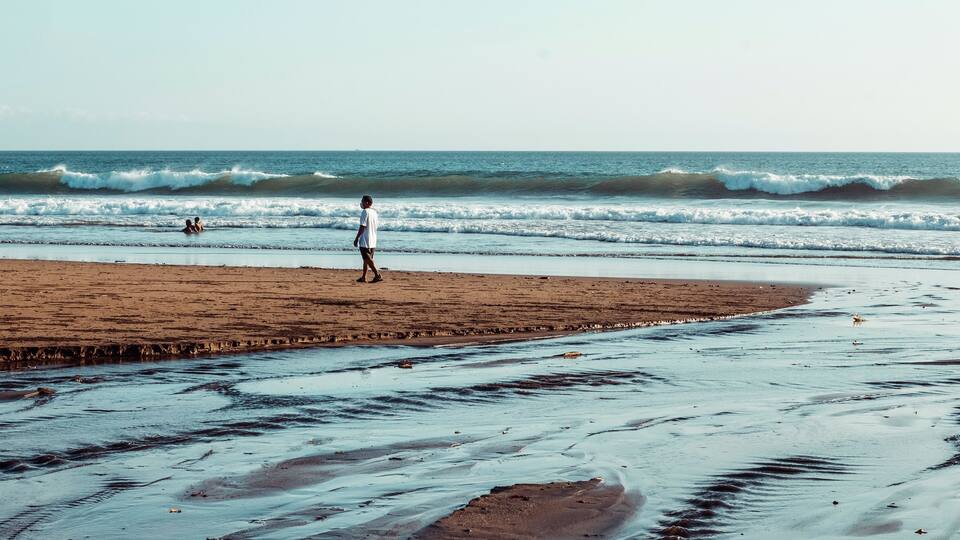A beach with waves, a person walking, and a sandy shore.