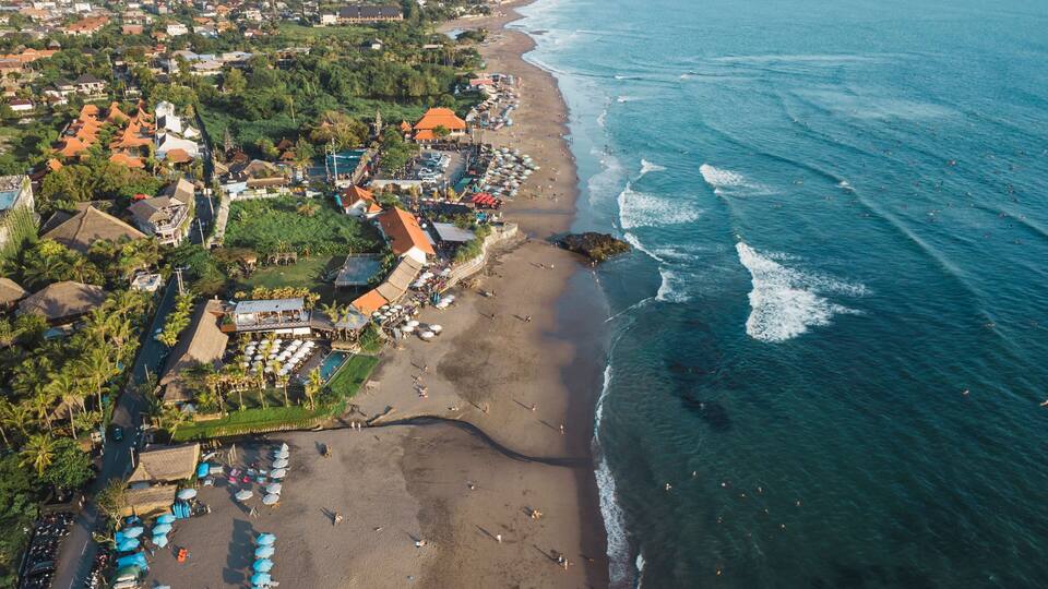 An aerial view of a coastal town with a beach, ocean, and residential area.