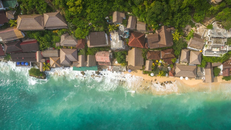 An aerial view of a coastal area with houses, a beach, and waves crashing onto the shore.