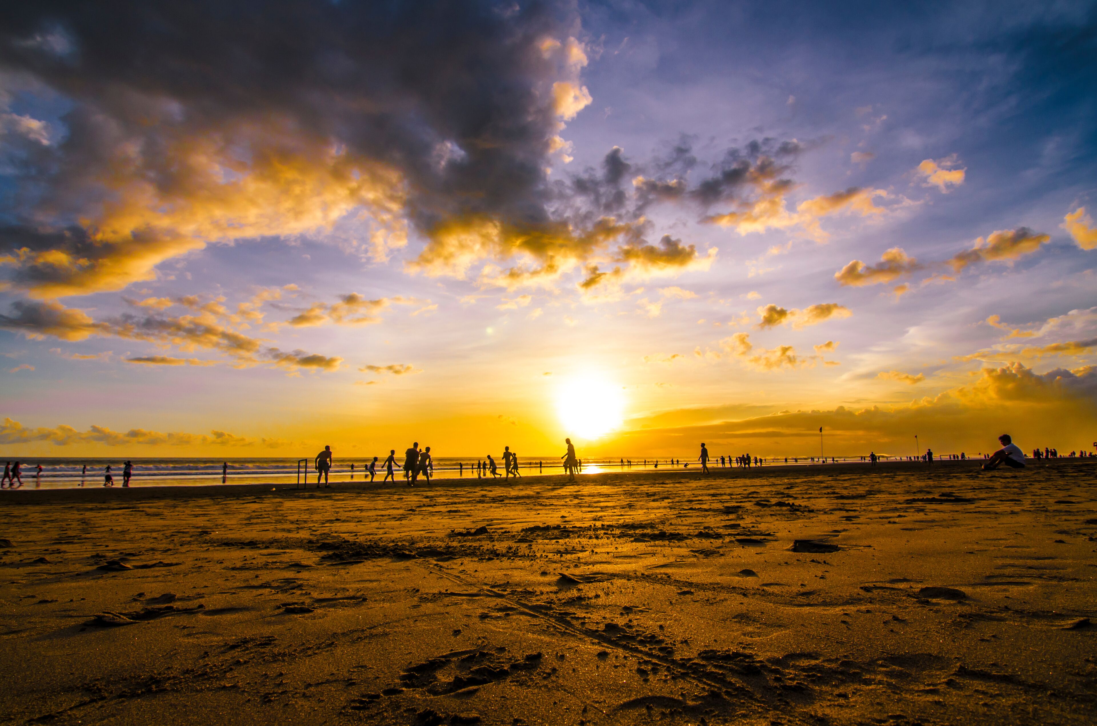 A beach with footprints, a sunset, and silhouettes of people.
