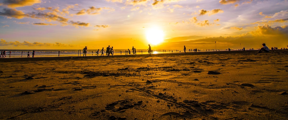 Una playa con huellas, un atardecer y siluetas de personas.