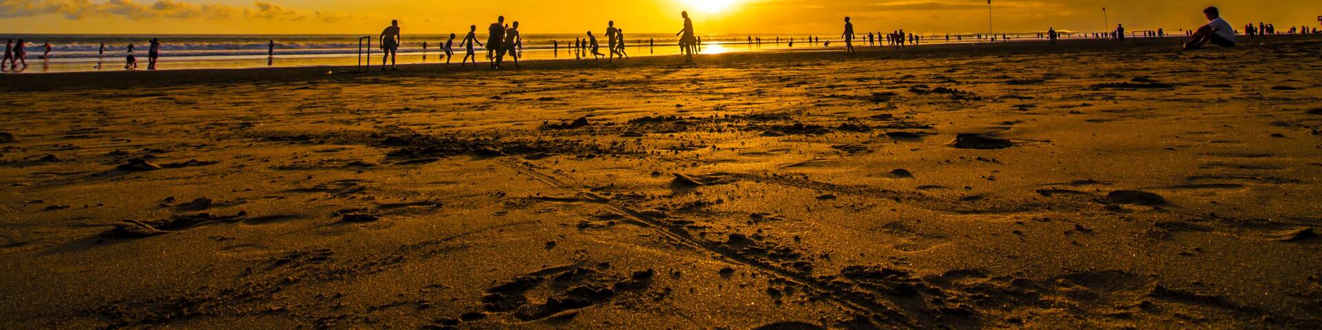 A beach with footprints, a sunset, and silhouettes of people.