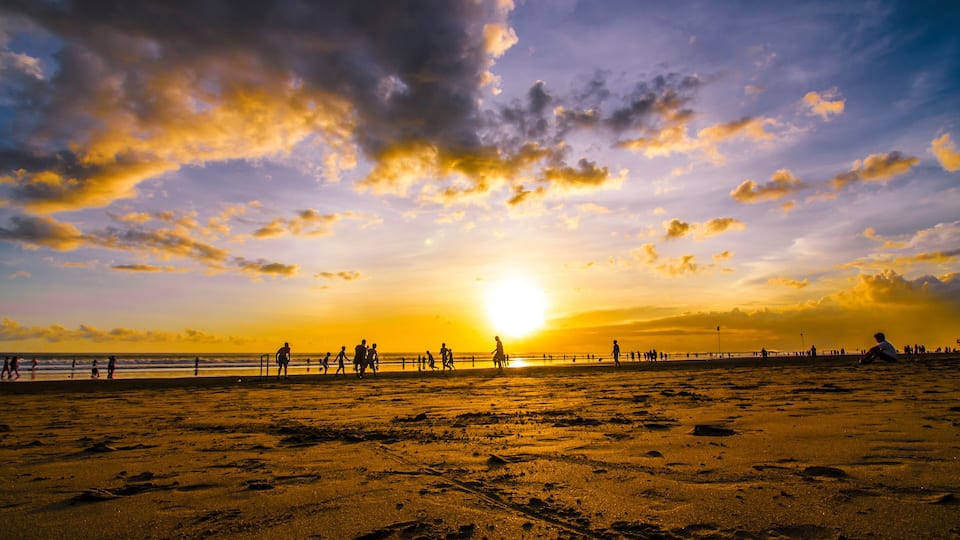 A beach with footprints, a sunset, and silhouettes of people.