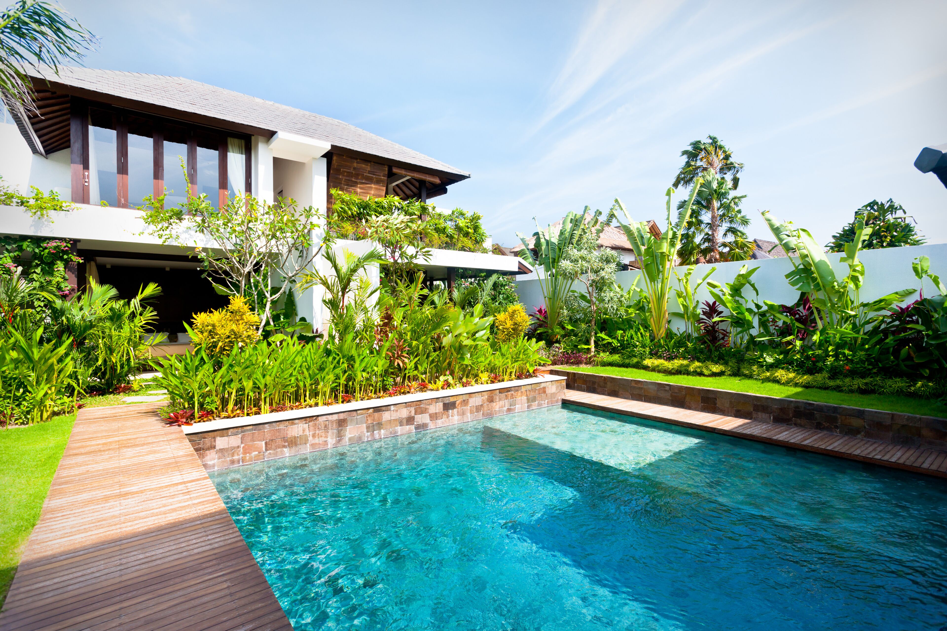 A modern house with a swimming pool, surrounded by lush greenery and a clear blue sky.