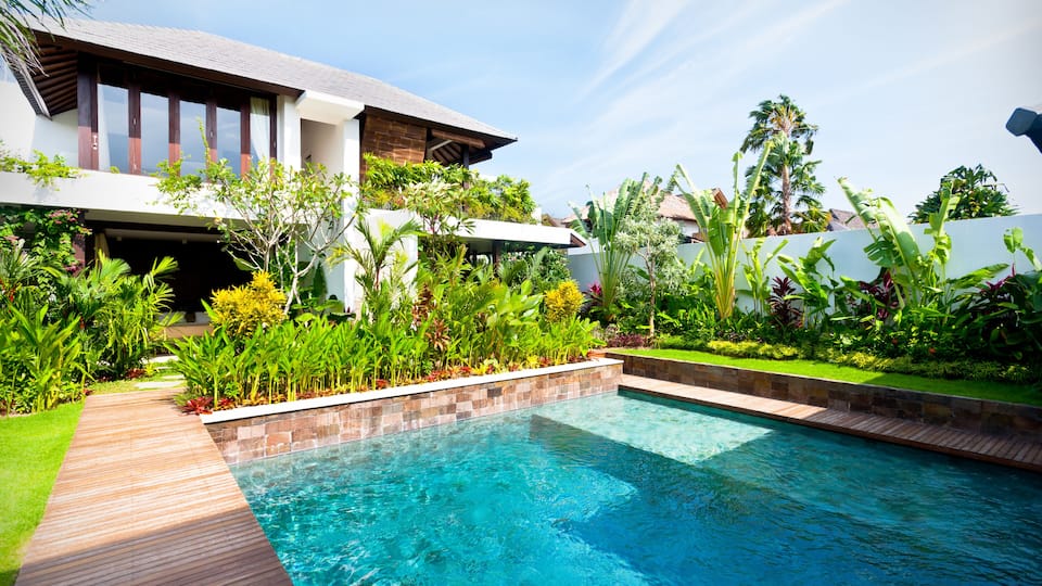 A modern house with a swimming pool, surrounded by lush greenery and a clear blue sky.