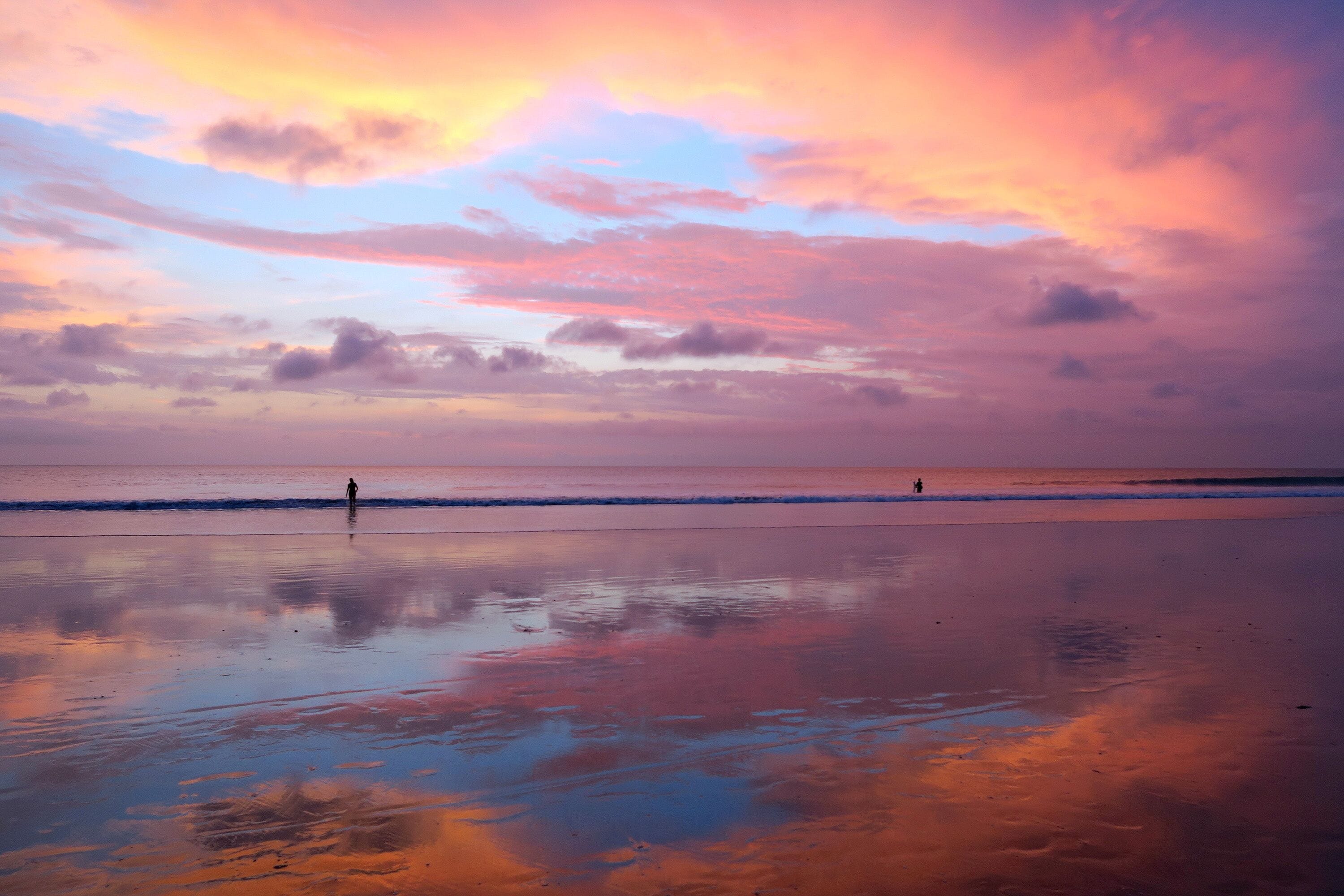 Beautiful Balinese sunset at Kuta beach with peoples and sky reflection in sand