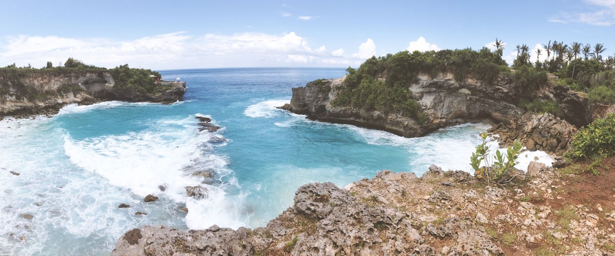A coastal landscape with rocky cliffs, clear blue waters, and lush greenery.