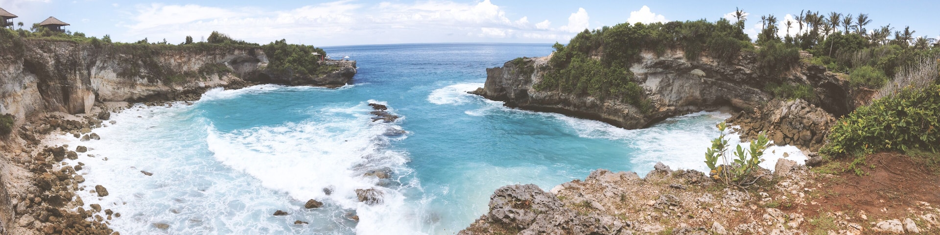 A coastal landscape with rocky cliffs, clear blue waters, and lush greenery.