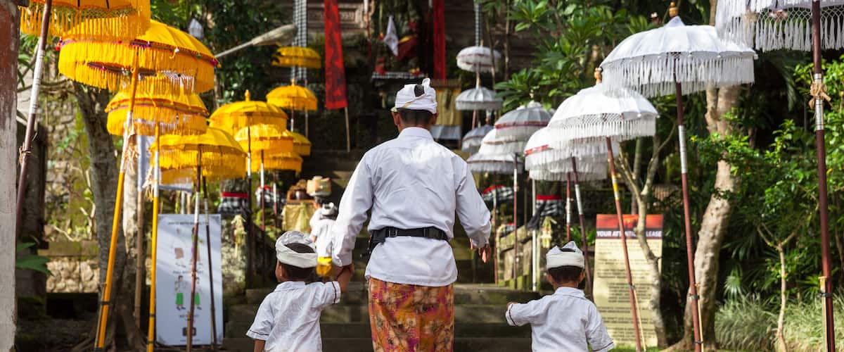 Un sendero bordeado por sombrillas tradicionales, una persona vestida de blanco y dos niños con atuendos iguales.