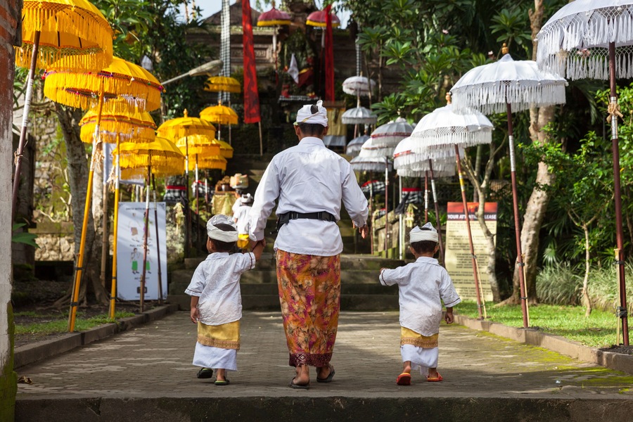 Un sendero bordeado por sombrillas tradicionales, una persona vestida de blanco y dos niños con atuendos iguales.