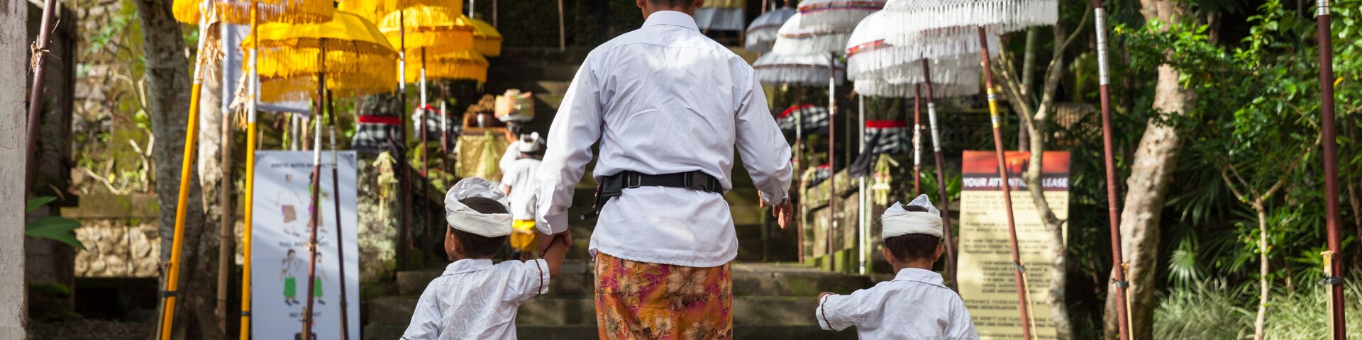 Un sendero bordeado por sombrillas tradicionales, una persona vestida de blanco y dos niños con atuendos iguales.