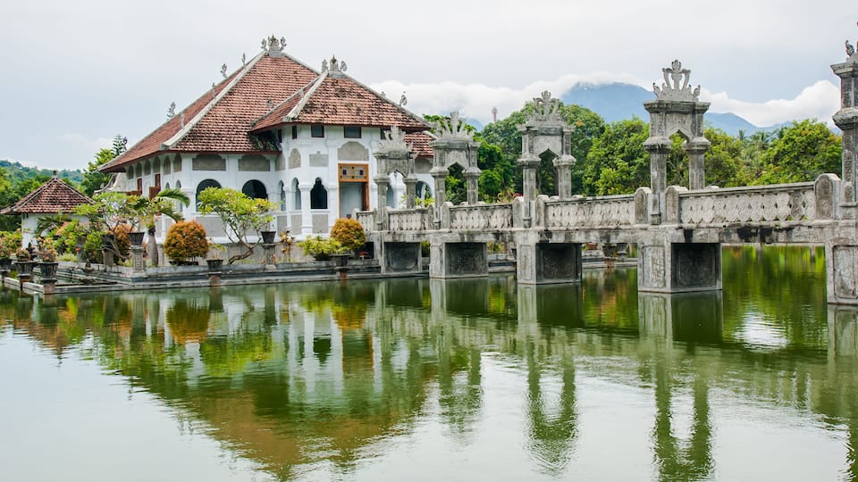 A traditional building with a tiled roof, a stone bridge, and a calm body of water reflecting the scenery.