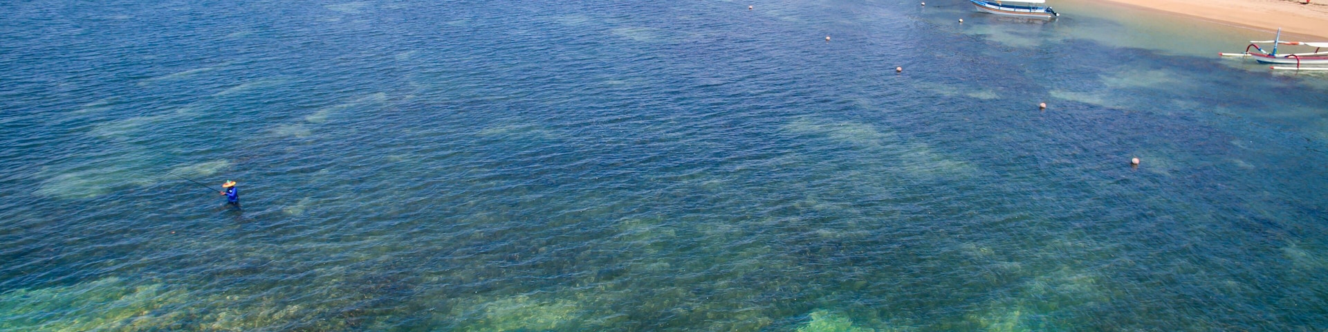A clear coastal area with a sandy beach, a small boat, and a person fishing.