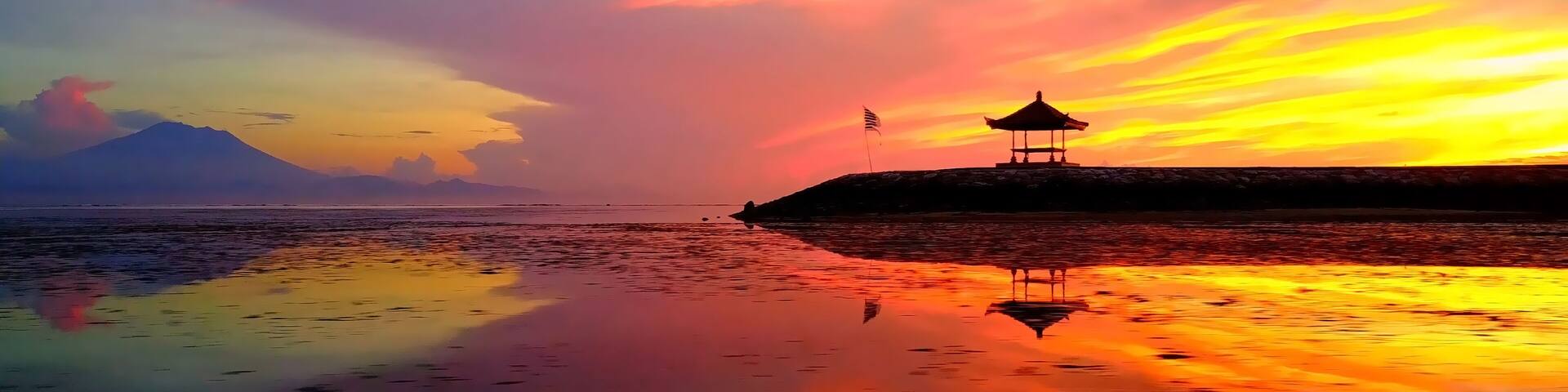 A sunset over a calm sea with a gazebo on a small island and a mountain in the background.