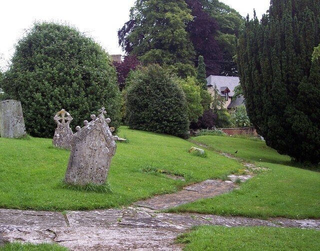 A cemetery with gravestones, a stone path, and lush greenery.