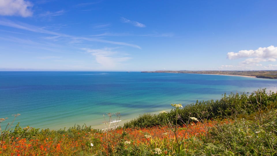 A coastal landscape with a clear blue sky, turquoise sea, and a sandy beach.