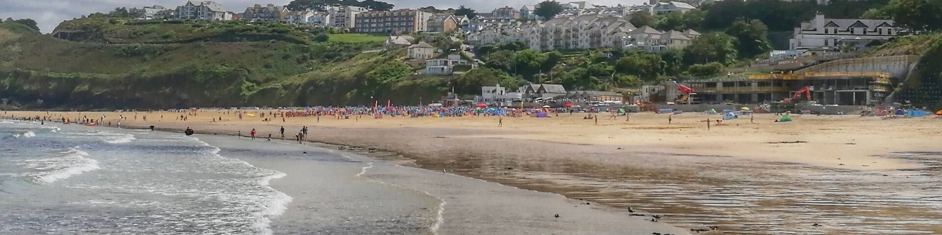 A beach with waves, people, and buildings in the background.